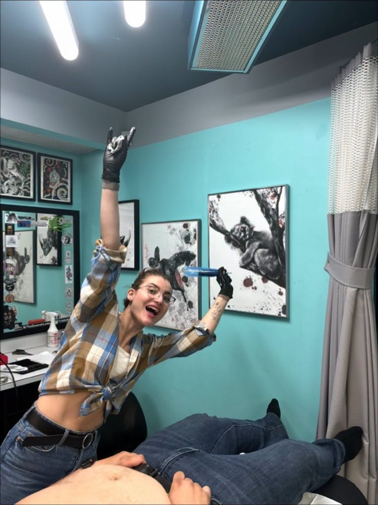 An artist tattooing a client at Strange World, turquoise walls and framed artwork behind