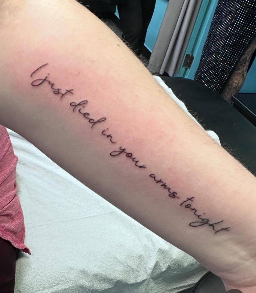 Fine line script lettering reading "I just died in your arms tonight", tattooed along a forearm by Abi Rojas
