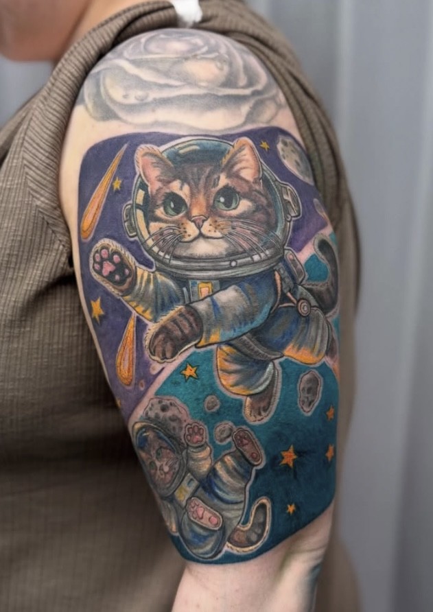 Full-colour astronaut cats floating in space, tattooed on an upper arm by Abi Rojas