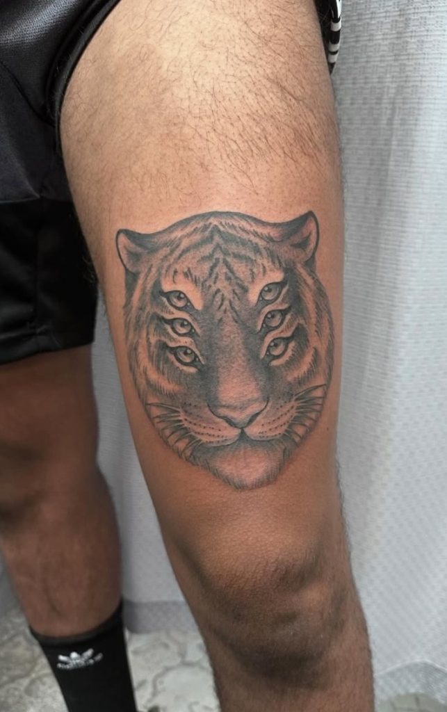 Black and grey six-eyed tiger head tattooed on a thigh by Abi Rojas