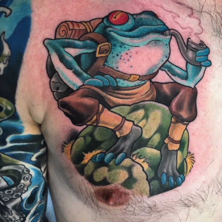 Full-colour neo-traditional frog with a pipe and pack, tattooed on the chest by Brett Schwindt